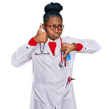 Young african american woman wearing doctor uniform and stethoscope doing thumbs up and down, disagreement and agreement expression. crazy conflict
