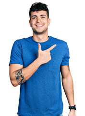 Young hispanic man wearing casual t shirt cheerful with a smile on face pointing with hand and finger up to the side with happy and natural expression