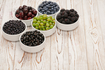 six bowls with seasonal berries, a mix of fresh berries on a wooden table