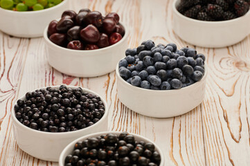 Ripe blueberries on the table in a plate, among the assortment of ripe berries, raspberries, blueberries, gooseberries, currants, shot close-up