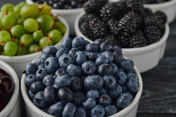 Ripe blueberries on the table in a plate, among the assortment of ripe berries, raspberries, blueberries, gooseberries, currants, shot close-up