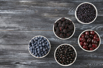 Ripe berries in bowls on a dark wooden background. dietary antioxidants and vitamins