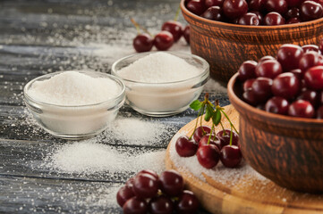 sugar for preservation in bowls on a wooden table, ripe cherries on the table