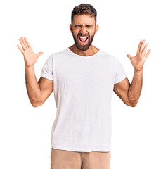 Naklejka premium Young hispanic man wearing casual white tshirt celebrating mad and crazy for success with arms raised and closed eyes screaming excited. winner concept