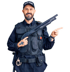 Young handsome man wearing police uniform holding shotgun smiling happy pointing with hand and...
