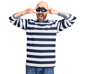 Young handsome man wearing burglar mask doing peace symbol with fingers over face, smiling cheerful showing victory