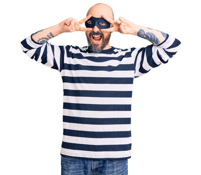 Young handsome man wearing burglar mask doing peace symbol with fingers over face, smiling cheerful showing victory