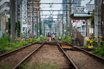 Tokyo Shitamachi trolly train (Toden) running in middle of city and two young asian girls walking across the tracks.