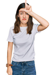 Young beautiful woman wearing casual white t shirt making fun of people with fingers on forehead doing loser gesture mocking and insulting.