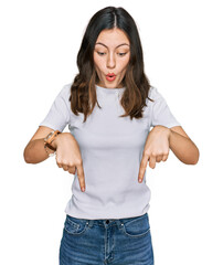 Young beautiful woman wearing casual white t shirt pointing down with fingers showing advertisement, surprised face and open mouth © Krakenimages.com