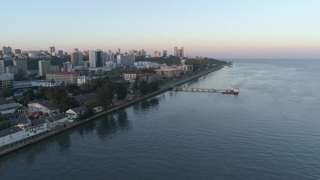 Aerial drone view of Avenida 10 de Novembro in Maputo City, Mozambique, capturing the coastal road curving along the Indian Ocean, with modern buildings, palm trees, and the vibrant waterfront 