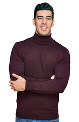 Handsome hispanic man wearing casual turtleneck sweater happy face smiling with crossed arms looking at the camera. positive person.