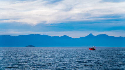 Red boat sailing on the lake towards a distant island between mountains