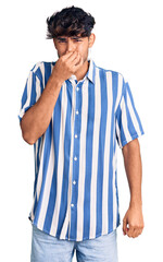 Young hispanic man wearing casual clothes smelling something stinky and disgusting, intolerable...