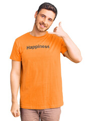 Handsome young man with bear wearing tshirt with happiness word message smiling doing phone gesture with hand and fingers like talking on the telephone. communicating concepts.