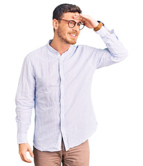 Handsome young man with bear wearing elegant business shirt and glasses very happy and smiling looking far away with hand over head. searching concept.