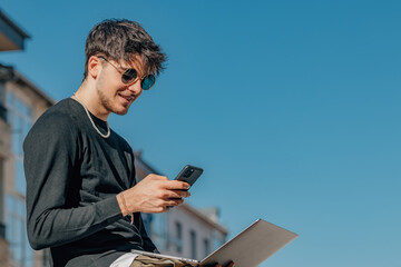 young man in the street outdoors with laptop and mobile phone