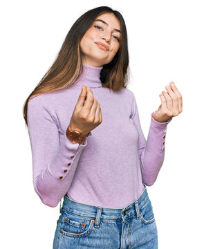 Young beautiful teen girl wearing turtleneck sweater doing money gesture with hands, asking for salary payment, millionaire business