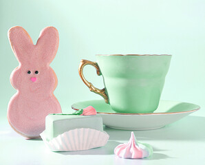 A Whimsical Easter Treat: A Pastel Green Teacup with a Gold Handle, a Bunny Rabbit Easter Cookie, A Pretty Pastel Cake and Meringue Candies