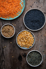 Various types of lentils (red, green, beluga) in bowls and plates on wooden background.