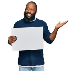 Young african american man holding blank empty banner celebrating victory with happy smile and winner expression with raised hands