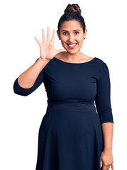 Young beautiful brunette woman wearing casual dress showing and pointing up with fingers number five while smiling confident and happy.