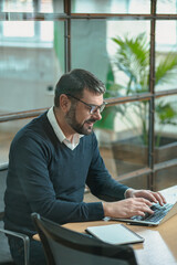 Busy man sitting at his desk, working on a laptop while typing