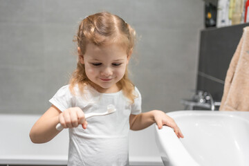 Happy toddler girl brushing teeth in the bath