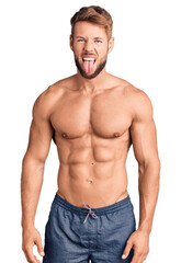 Fototapeta premium Young caucasian man standing shirtless sticking tongue out happy with funny expression. emotion concept.