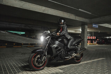 Fototapeta na wymiar Young woman biker in a helmet sitting on a motorcycle in the underground parking garage