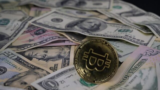 Slow rotation of a bitcoin coin on dollar banknotes. Bitcoin shines in the light during the rotation and beautifully falls on the dollars with an up sign. Bitcoin and dollars concept.