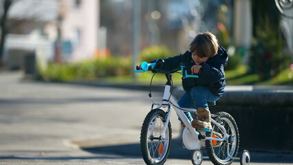 Naklejka premium Child riding bicycle during winter season outside at city park. Kid cyclist learning to ride bike
