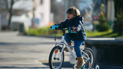 Child riding bicycle during winter season outside at city park. Kid cyclist learning to ride bike