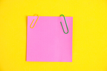 Bright pink sticker for notes and paper clips yellow background.
