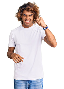 Young hispanic man wearing casual white tshirt angry and mad raising fist frustrated and furious while shouting with anger. rage and aggressive concept.