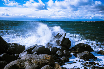 Waves of the Mediterranean Sea which with foam and splashes break against huge stones on the shore, Cagliari, Sardinia, Italy