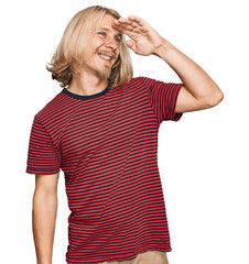 Caucasian man with blond long hair wearing casual striped t shirt very happy and smiling looking far away with hand over head. searching concept.