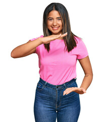 Obraz premium Young latin girl wearing casual clothes gesturing with hands showing big and large size sign, measure symbol. smiling looking at the camera. measuring concept.