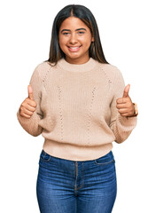 Young latin girl wearing wool winter sweater success sign doing positive gesture with hand, thumbs up smiling and happy. cheerful expression and winner gesture.