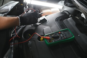 Car mechanic is using a multimeter with voltage range measurement to check the voltage level of the...