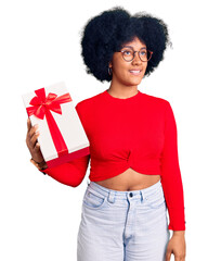 Young african american girl holding gift smiling looking to the side and staring away thinking.