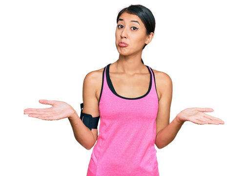 Beautiful asian young sport woman wearing sportswear and arm band clueless and confused expression with arms and hands raised. doubt concept.