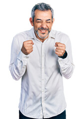 Fototapeta premium Middle age hispanic with grey hair wearing casual white shirt excited for success with arms raised and eyes closed celebrating victory smiling. winner concept.