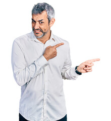 Middle age hispanic with grey hair wearing casual white shirt pointing aside worried and nervous with both hands, concerned and surprised expression