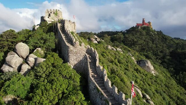 Aerial view of the town of Sintra in Portugal, historical Castelo Dos Mouros (moors castle) fortress, walls and Pena Palace in the summer, taken with a drone, on a beautiful green summit rocky hilltop