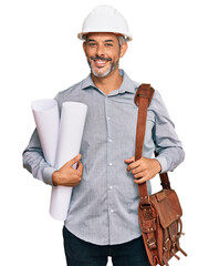 Middle age grey-haired man wearing safety helmet holding blueprints looking positive and happy...