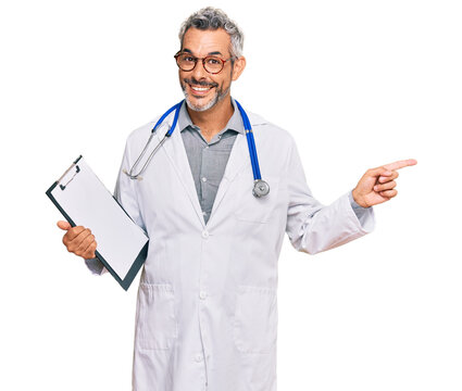 Middle age grey-haired man wearing doctor stethoscope holding clipboard smiling happy pointing with hand and finger to the side