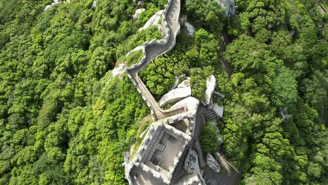 Aerial view of the town of Sintra in Portugal, historical Castelo Dos Mouros (moors castle) fortress, walls and Pena Palace in the summer, taken with a drone, on a beautiful green summit rocky hilltop