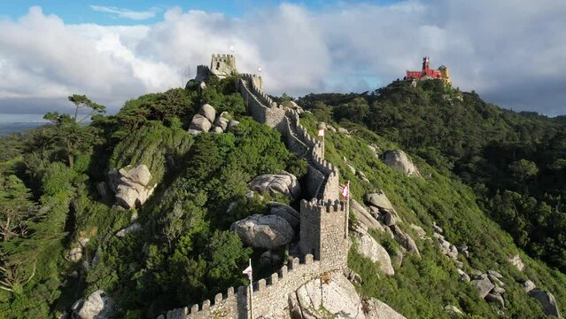 Aerial view of the town of Sintra in Portugal, historical Castelo Dos Mouros (moors castle) fortress, walls and Pena Palace in the summer, taken with a drone, on a beautiful green summit rocky hilltop