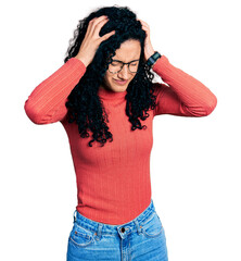 Young hispanic woman with curly hair wearing glasses suffering from headache desperate and stressed...